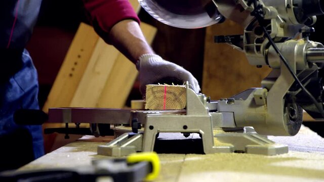 A joiner cuts off a piece of wood blank using a circular saw with a laser in the workshop. Work with miter saw for cutting boards and bars. Renovation with professional construction and repair tool.