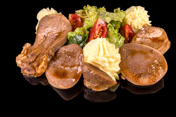 A delicious beef tongue with mashed potatoes and fresh salad, with reflection, isolated on black background