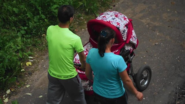 A man and a woman are walking down the street and pushing a baby stroller. The view from the top. Slow motion images