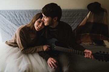Romantic and happy caucasian couple in casual wedding clothes spending the morning together. Love, relationships, romance, happiness, urban concept. Man and woman hugging and playing the guitar.