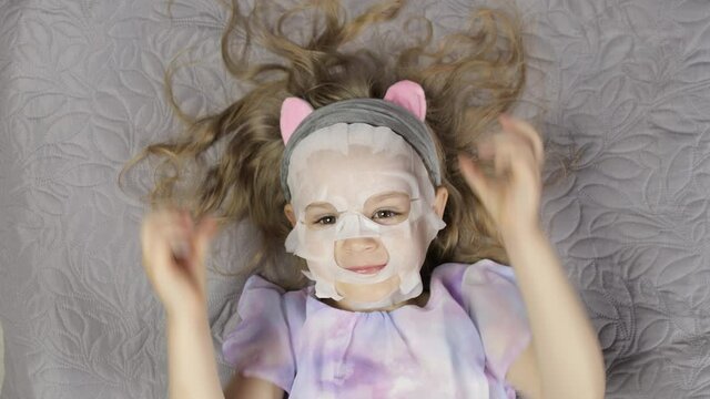 Teen girl applying moisturizing face mask. Child kid take care of skin with cosmetic facial mask