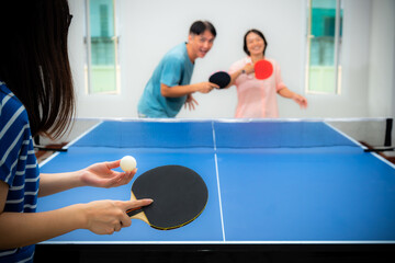 Couple fun playing table tennis or Ping pong indoor together leisure with competing in sports games at house. Father mother and daughter Asian family enjoy recreation exercise stay at home in Thailand