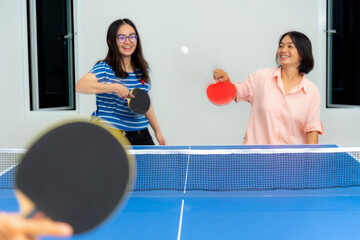 Asian family fun playing table tennis or Ping pong indoor together leisure with competing in sports games in the house. Mother and daughter enjoy recreation or exercise stay at home in Thailand