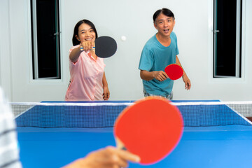 Couple active fun playing table tennis or Ping pong indoor together leisure with competing in sports games in the house. Asian family enjoy recreation or exercise stay at home in Thailand