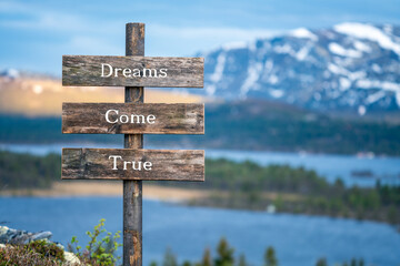 dreams come true text on wooden signpost outdoors in landscape scenery during blue hour and sunset.