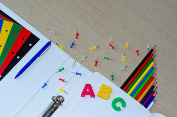 Colorful composition of vibrant color school supplies: colored pencils, papers, pens and english letters on the withe wooden background. Copy space. Flat lay. Back to school and education concept.