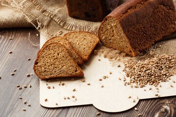 Bread in form of triangle and with sunflower seeds near spikelets of wheat lies on old weathered wooden table. Rustic bread and wheat on an old vintage planked wood table. Free text space.