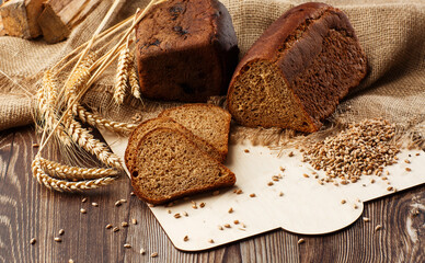Bread in form of triangle and with sunflower seeds near spikelets of wheat lies on old weathered wooden table. Rustic bread and wheat on an old vintage planked wood table. Free text space.