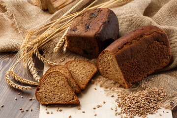 Bread in form of triangle and with sunflower seeds near spikelets of wheat lies on old weathered wooden table. Rustic bread and wheat on an old vintage planked wood table. Free text space.