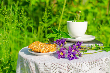 Table in the garden with a cup of green tea and flowers, covered with a lace white tablecloth. Evening tea with cookies. Summer village concept. Copy space.