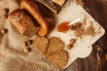 Bread in form of triangle and with nuts and honey near spikelets of wheat lies on old weathered wooden table. Rustic bread and wheat on an old vintage planked wood table. Free text space.