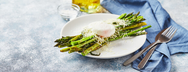 Green asparagus with poached egg and parmesan, vegetarian breakfast served on white plate on light...