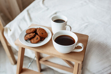 Breakfast in bed. Hot coffee with oatmeal cookies with chocolate on a wooden tray.