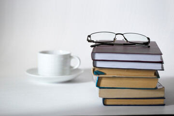 Glasses on  books on a white background with a white cup of coffee