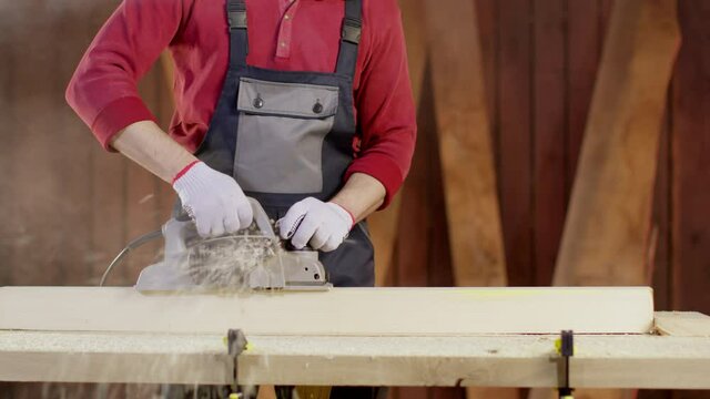 Close-up of work with an electric planer. Polishing of wooden products, wood shavings and sawdust fly apart and smoke comes. Home furniture manufacturing concept. Professional repair tool.