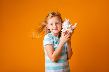 Portrait of a little blonde girl holds a sea shell near her ear on a yellow background, space for text