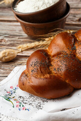 Homemade Jewish traditional challah bread on white napkin on wooden table. Homemade Decorated with poppy seeds. Jewish cuisine. Copy space for text, brand or logo. Close up and top view