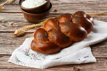 Homemade Jewish traditional challah bread on white napkin on wooden table. Homemade Decorated with poppy seeds. Jewish cuisine. Copy space for text, brand or logo. Close up and top view