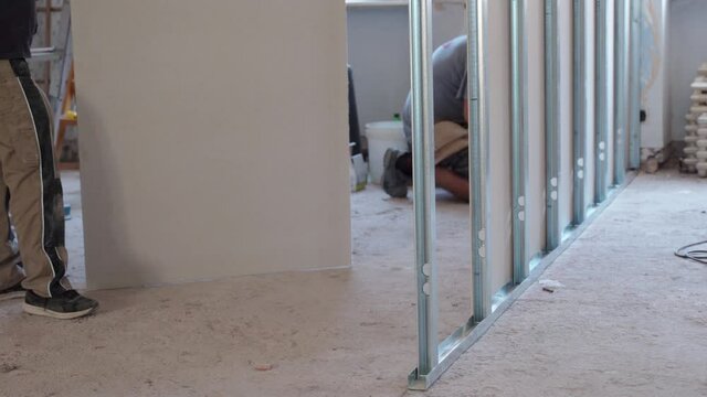 Process of drywalls installation on horizontal and vertical metal profiles on construction site. Building workers assembling plasterboards, remodeling walls and doing interior reconstruction. Teamwork