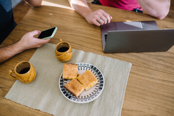 People, laptop, phone and breakfast on a wooden table.