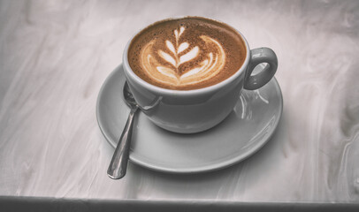 Cappuccino coffee cup at trendy cafe with latte art in foam on top of espresso drink in trendy blue mug on tabletop.