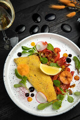 breaded sea fish fillet. With vegetable garnish. On a dark wooden table.
