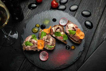 Meat bruschettas with cheese, vegetables, on a dark stone board
