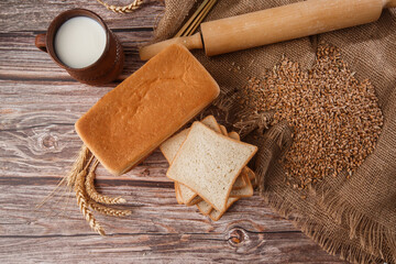 Close-up of homemade bread. Peasant square bread and wheat spikelets with space for text. Homemade baking. White bread with flour and milk on wooden chopping board wheat rye ears copy space.