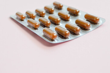 blister with brown tablets for the treatment of disease. pack of oblong-shaped tablets on a pink background. medicines for maintaining and health of the human body and animals