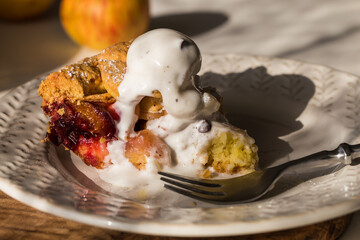 Piece of traditional apple pie with vanilla ice cream, and whole pie in ceramic baking form on white kitchen.