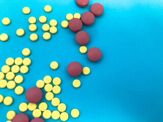 round pink and yellow volumetric tablets on a blue paper non-glossy background. drugs to strengthen the immune system. natural products poured from packaging. medical background