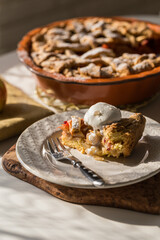 Piece of traditional apple pie with vanilla ice cream, and whole pie in ceramic baking form on white kitchen.