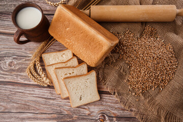 Fototapeta na wymiar Close-up of homemade bread. Peasant square bread and wheat spikelets with space for text. Homemade baking. White bread with flour and milk on wooden chopping board wheat rye ears copy space.