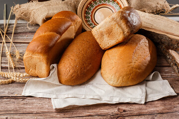 Different kinds of fresh bread as background, top view. Bakery gold rustic crusty loaves of bread and buns on wooden background. Still life captured from above. Kitchen or bakery poster design.