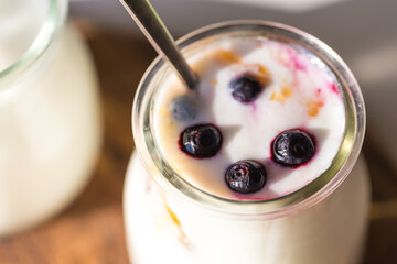  Glass jar with natural homemade yogurt with frozen bilberries and apricot jam on white background .