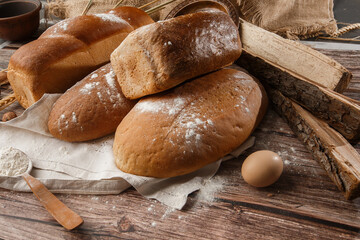 Different kinds of fresh bread as background, top view. Bakery gold rustic crusty loaves of bread and buns on wooden background. Still life captured from above. Kitchen or bakery poster design.