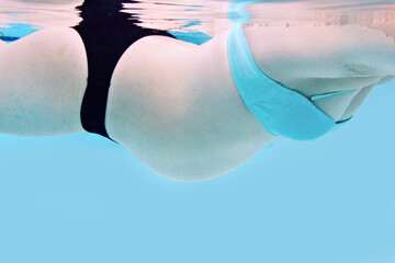 Pregnant woman with baby belly swimming in a pool, underwater capture