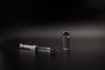Small vaccine bottle and a medical syringe isolated on black background