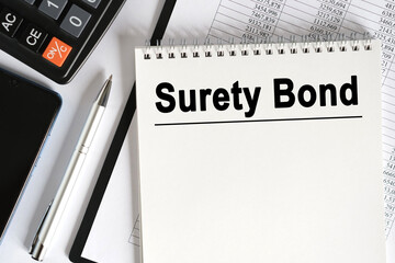 On the table lies a smartphone, a calculator and a notebook with the inscription- Surety Bond.