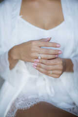 A young bride in a silk dressing gown sits and straightens an engagement and wedding ring on her hand.