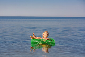 a small child swims across the sea in an inflatable circle and looks up. 