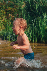 Fototapeta premium Boy baby runs in the water cheerful and contented, sprays fly in all directions