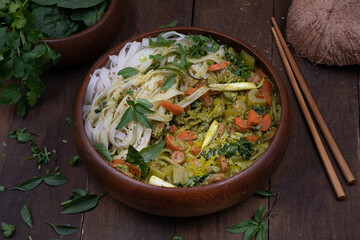 Vegan Thai green curry and rice noodles served in wooden bowl on wooden table