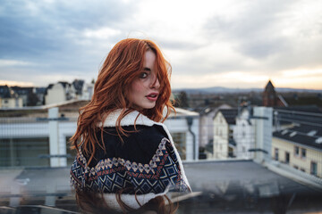 Beautiful millennial girl standing on terrace and looking over shoulder to camera. Attractive...