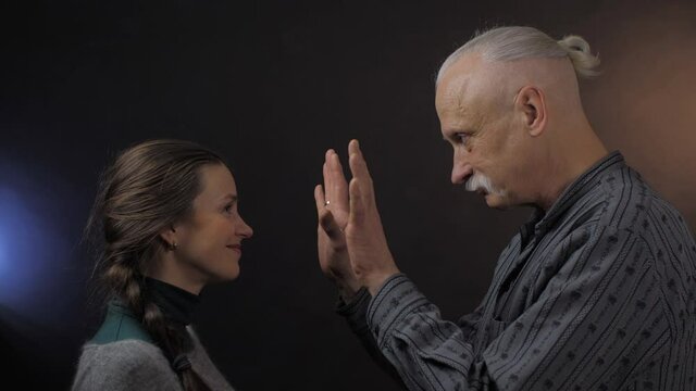 happy elderly man with grey hair bun and pretty woman with braid imitate pantomime moves with hands close view. Concept people emotion