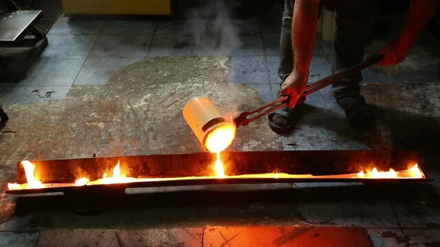 Molten silver being poured from a crucible into an ingot mold with the light coming from the molten silver.