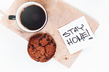 Chocolate brownie cookies, coffee cup, and sticky note STAY HOME Pandemic Covid-19 Coronavirus quarantine concept for social distancing awareness, top view