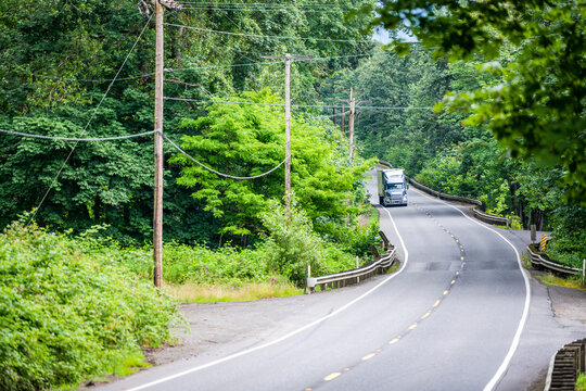 Industrial Diesel Big Rig Gray Semi Truck With Semi Trailer Running On The Winding Forest Road With Phone And Electric Power Poles