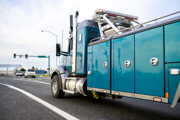 Powerful heavy-duty big rig towing semi truck running on the city street with traffic light going to help broken semi trucks