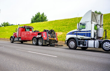 Red big rig semi towing truck prepare to tow broken white big rig semi tractor standing out of...